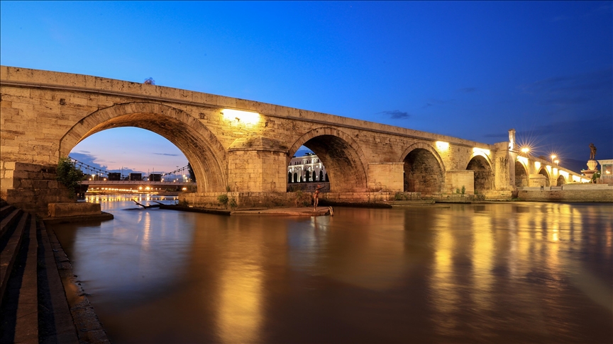 Осветен камен мост навечер, одразен во смирена река